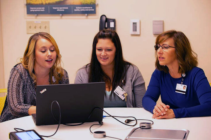 Three females look at a laptop sitting at a table.